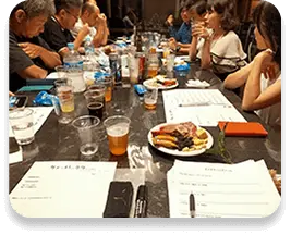 様々なビールをテーブルに並べ、人が話したり、メモを取ったりしている写真